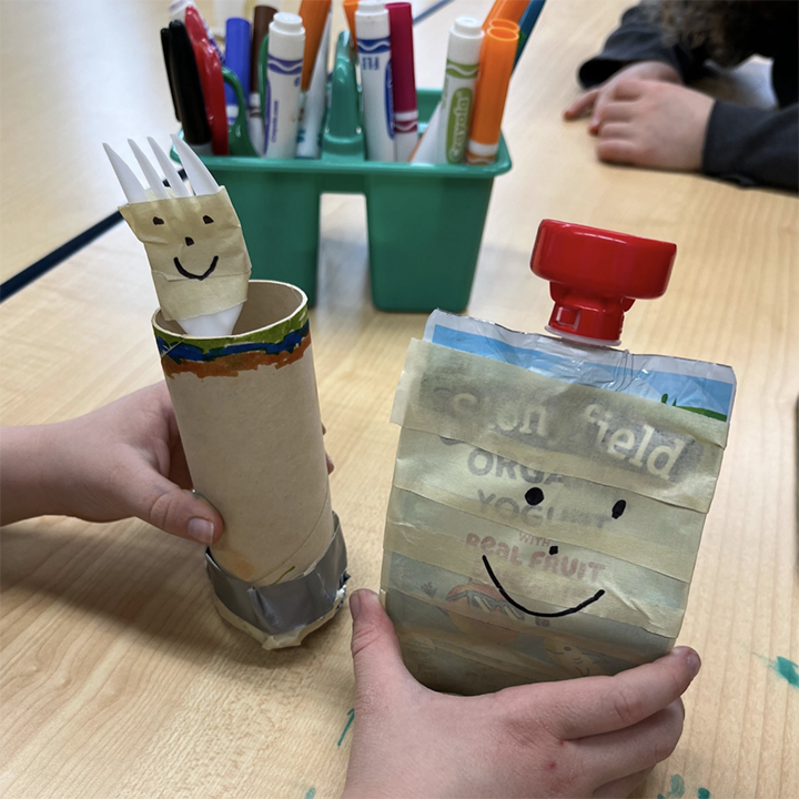 A yogurt pouch, fork, and empty toilet paper roll are recycled into toys with tape and smiles.